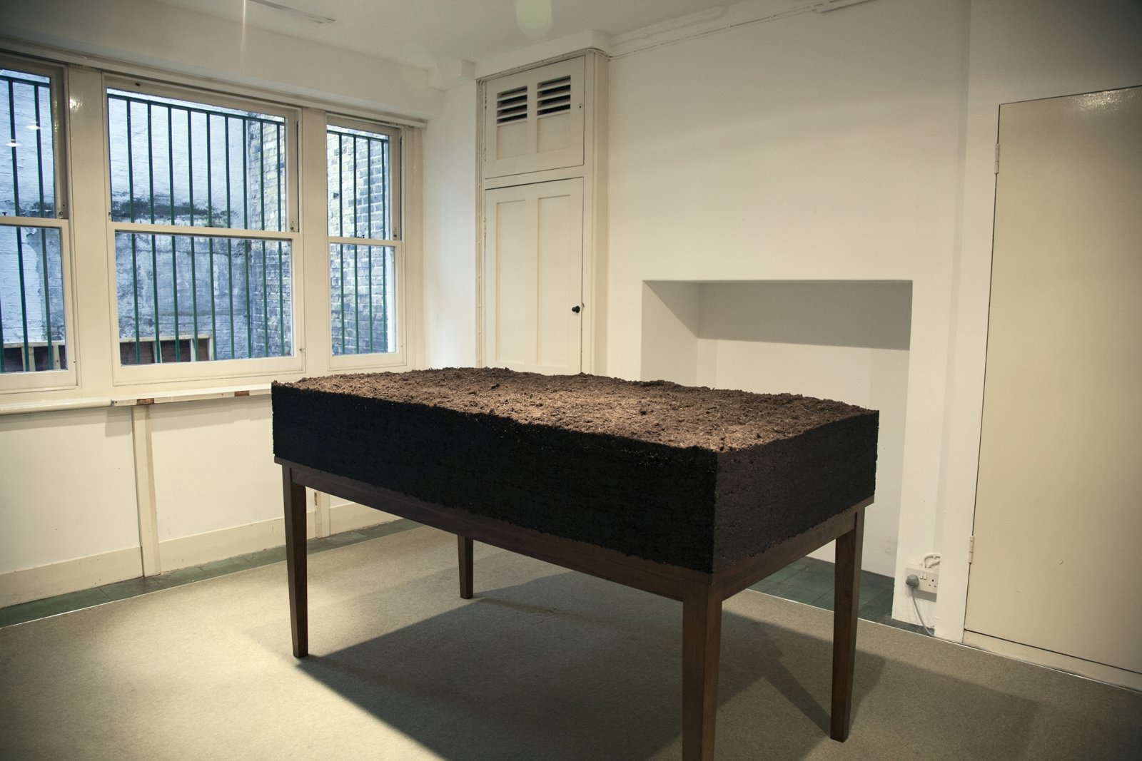 Abbas Akhavan, Dirt/Table, 2012, topsoil, water, wooden table, 42 x 36 x 72 in. (106 x 91 x 182 cm). Installation view, Study for a Garden, Delfina Foundation, London, UK, 2012