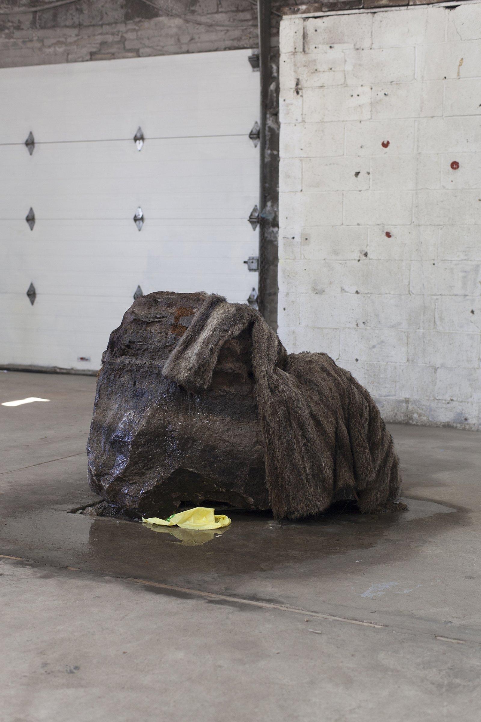 Abbas Akhavan, Untitled, 2018, erratic boulder, water system, vintage fur coat, plastic bag, 40 x 30 x 31 in. (102 x 75 x 80 cm). Installation view, Folly, Vie d’ange, Montreal, 2018