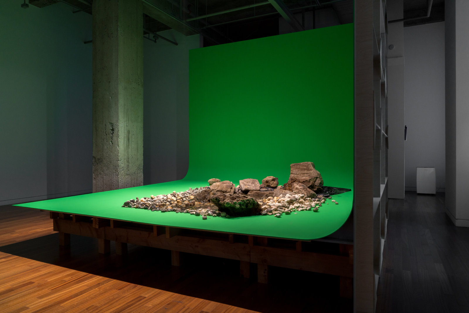 Abbas Akhavan, spill, 2021, boulders, rocks, river stones, water, PVC pond membrane, water pumps and tubing, pressure treated lumber, baltic birch plywood, various hardware, chroma key paint, full spectrum L.E.D. lightbulbs, 144 x 144 x 144 in. (366 x 366 x 366 cm). Installation view, Sensing Nature, Momenta Biennale at Phi Foundation for Contemporary Art, Montreal, Canada