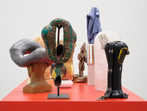Valérie Blass, L’érotisme du ventriloque / The erotic ventriloquist ﻿(detail), 2024, mask stand, wooden head, glass bell, sweaters, log hook, candlestick, porous stone carved in the shape of a dog, moth, ceramic kiln brick, driftwood, burnt wood, belt, di