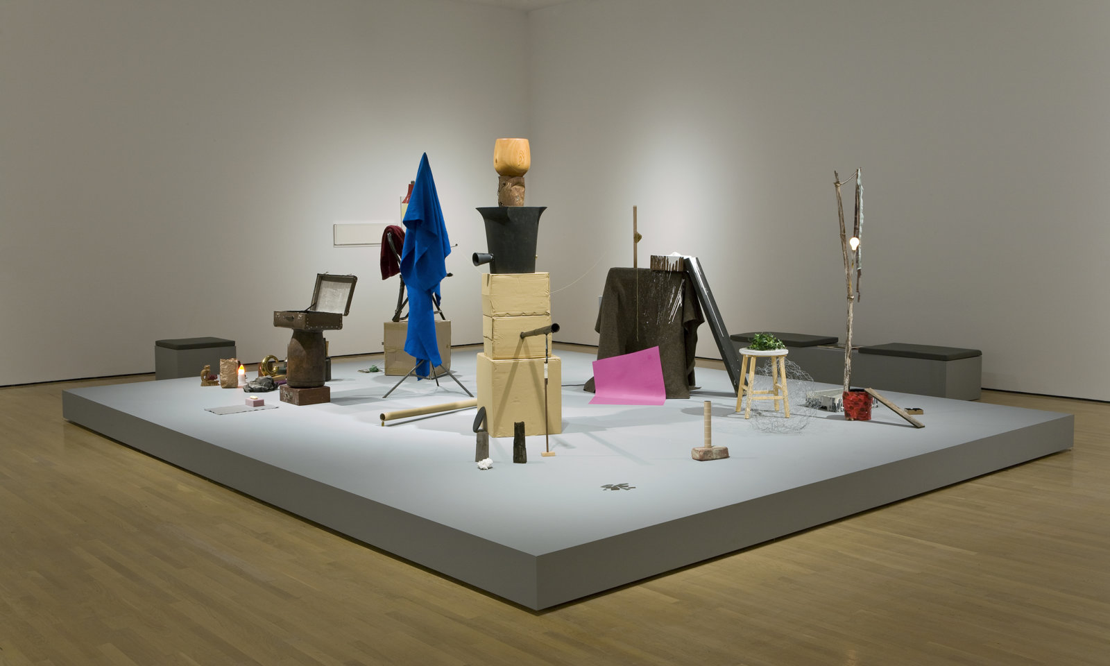 Geoffrey Farmer, And Finally the Street Becomes the Main Character (Clock), 2005–2008, wooden stage, computer controlled soundscape, 8 speakers, styrene brick, glass shards, paint can, tree branch, paint tray, stool, artificial ivy, hand carved wooden bowl, cardboard boxes, wooden mallet, protest sign, cardboard tubes, leather suitcase, folding chair, towel, sweater, desk lamp, string, blanket, light bulbs, tripod, sponge, lock box, tissue, paper bag, oil can, moth, thread, masking tape, felt, books, rag, wooden figure, spoon, paint, styrene cup, chopstick, candleholder, ballet costume, brass sculpture, found wood, various framed works, dimensions variable