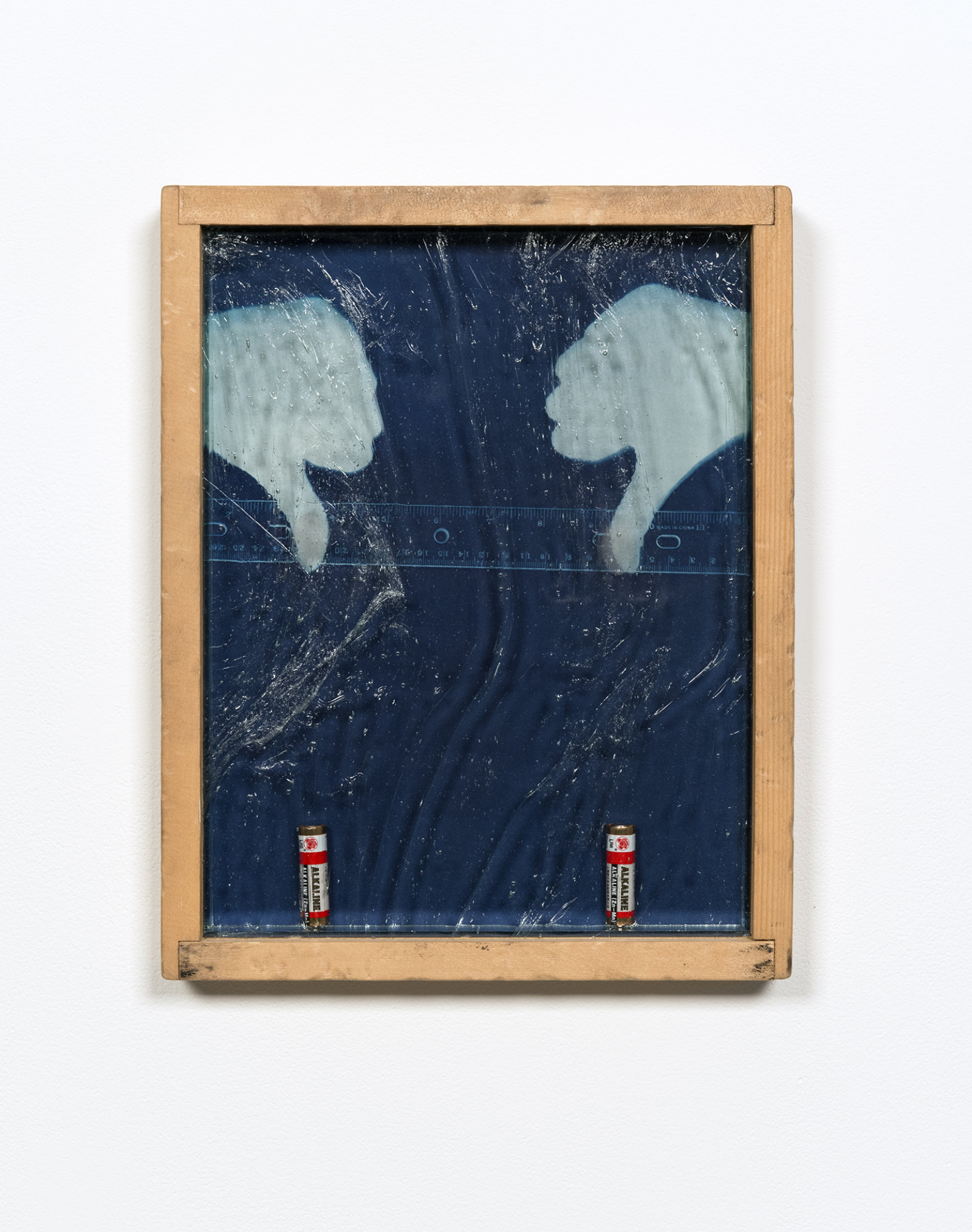 Kasper Feyrer, Rule of thumbs: Double Negative, 2012, antiqued/distressed pine wood frame (beaten with chain, orange pekoe stain), cyanotype on watercolour paper, two dead aa alkaline batteries, magnets, mirror inset, “alte deutsch” architectural glass, thumb fingerprints dusted with bi-chromatic fingerprint powder, 15 x 12 in. (39 x 30 cm)