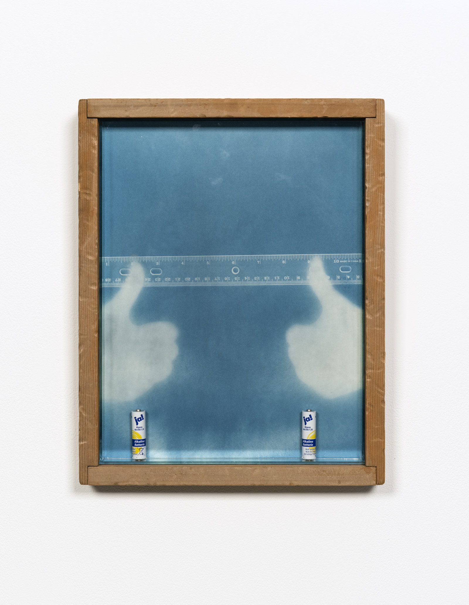 Kasper Feyrer, Rule of thumbs: Double Positive, 2012, antiqued/distressed pine wood frame (beaten with chain, iron oxide stain), cyanotype on watercolour paper, two dead a alkaline batteries, magnets, mirror inset, “new german antique” architectural glass, thumb fingerprints dusted with bi-chromatic fingerprint powder, 15 x 12 in. (38 x 30 cm)