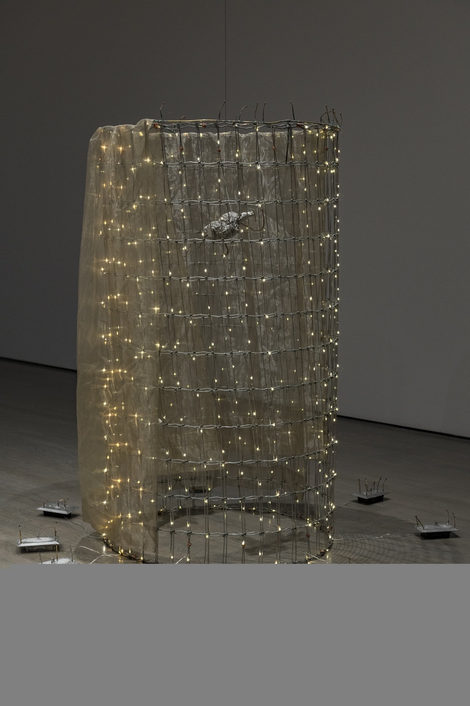Rochelle Goldberg, Trigger: Towards everything they’ve ever wanted, 2019, ranch fencing, batteries, fairy lights, polyester curtain, aluminum, cast bronze matches, copper wire, 51 x 51 x 44 in. (130 x 130 x 112 cm). Installation view, In the No Longer Not Yet, Leonard and Bina Ellen Art Gallery, Montreal, 2020
