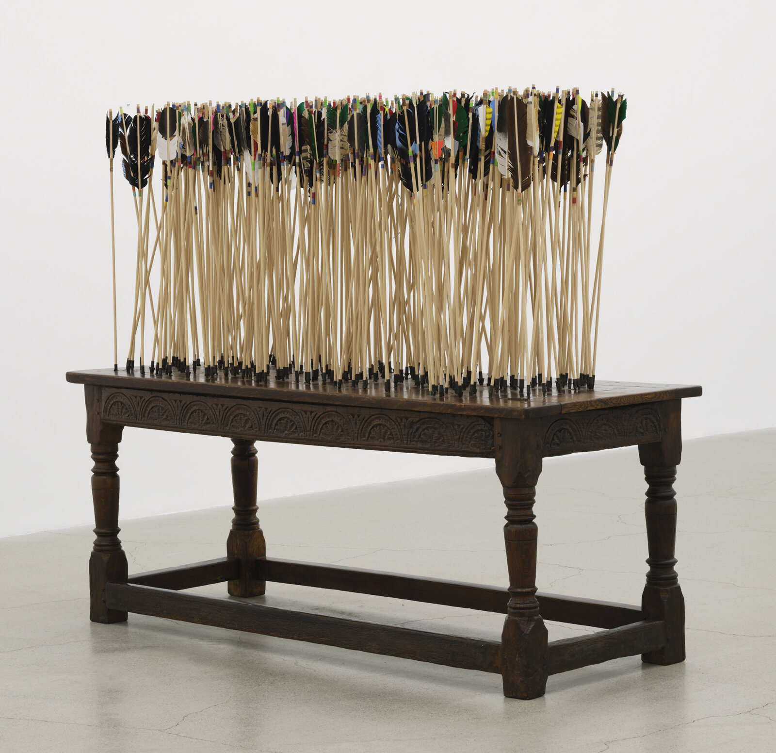 Brian Jungen, The Way of the World, 2024, 250-year-old French colonial oak table from Baton Rouge, wood arrows, carbon steel points, feather, artificial sinew, 63 x 76 x 29 in. (160 x 193 x 74 cm)