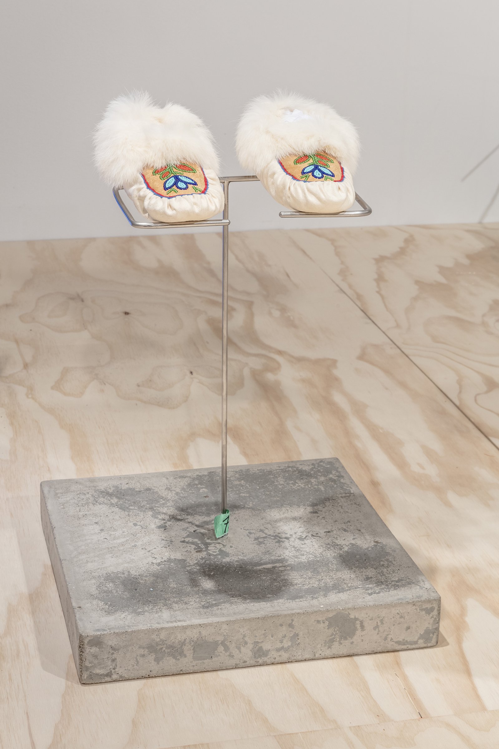 Duane Linklater, Speculative apparatus 1 for the work of nohkompan, 2016, concrete, welded stainless steel, tape, 16 x 16 x 19 in. (41 x 41 x 48 cm), with Beaded Slippers, c. 1980, by Ethel Linklater from the Collection of Thunder Bay Art Gallery, moosehide, caribou hide, rabbit fur, beads, 9 x 4 in. (23 x 9 cm). Installation view, From Our Hands, Mercer Union, Toronto, 2016