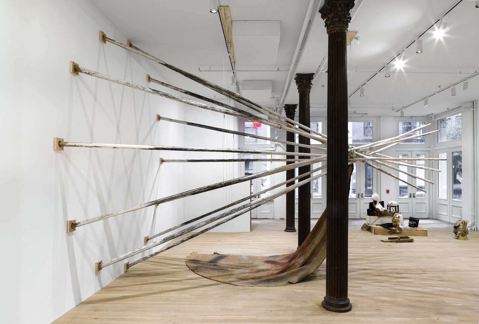 Duane Linklater, dislodgevanishskinground, 2019, 12 teepee poles, steel cable, white paint, charcoal, rope, digital print on linen, black tea, blueberry extract, sumac, charcoal, 220 x 174 x 174 in. (559 x 442 x 442 cm). Installation view, Artists Space, New York, USA, 2019