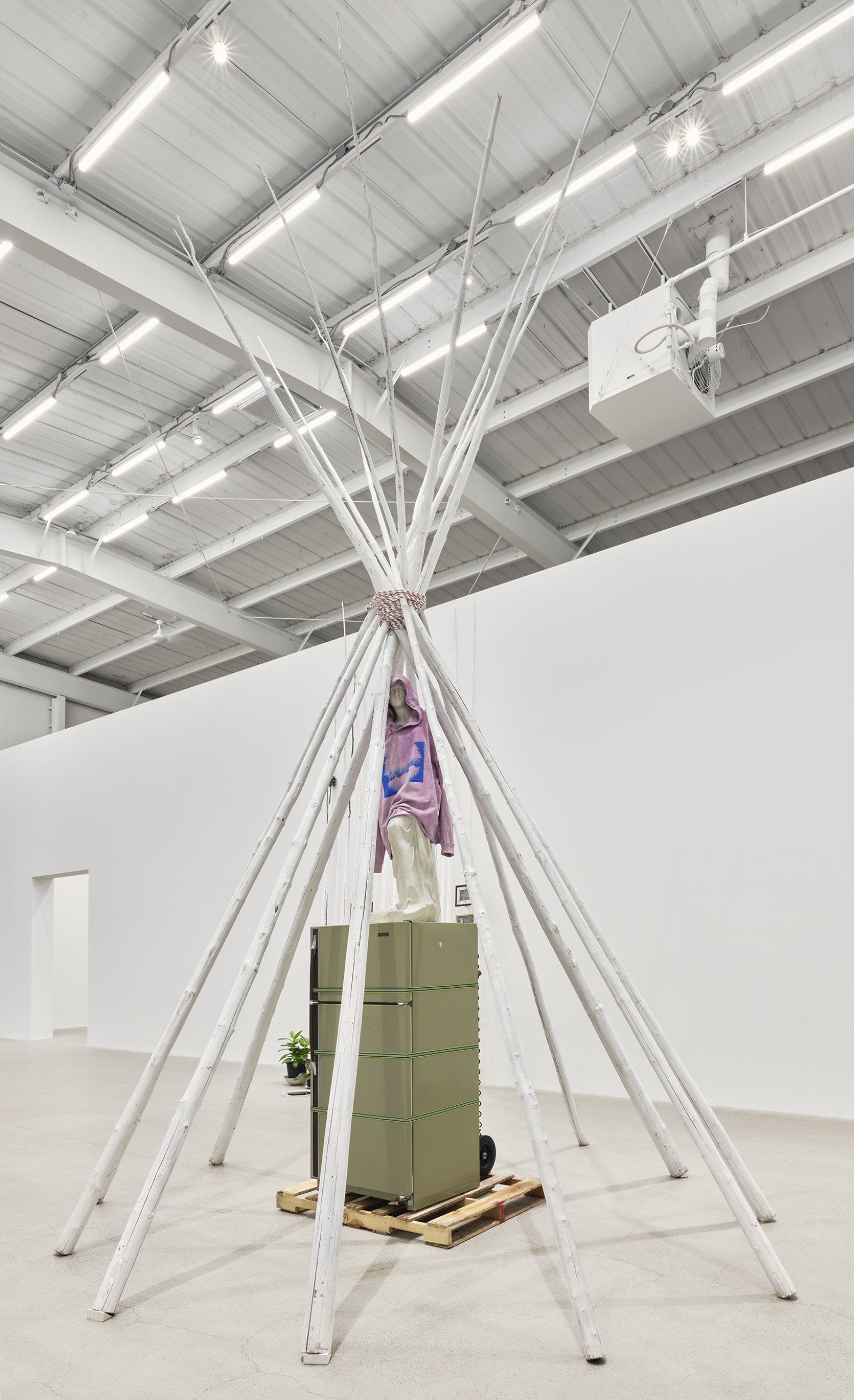 Duane Linklater, what grief conjures, 2020, teepee poles, paint, nylon rope, wooden pallet, refrigerator, tie-down straps, hand truck, plastic statue, handmade hoodie, cochineal dye, silkscreen, 249 x 160 x 160 in. (632 x 406 x 406 cm)