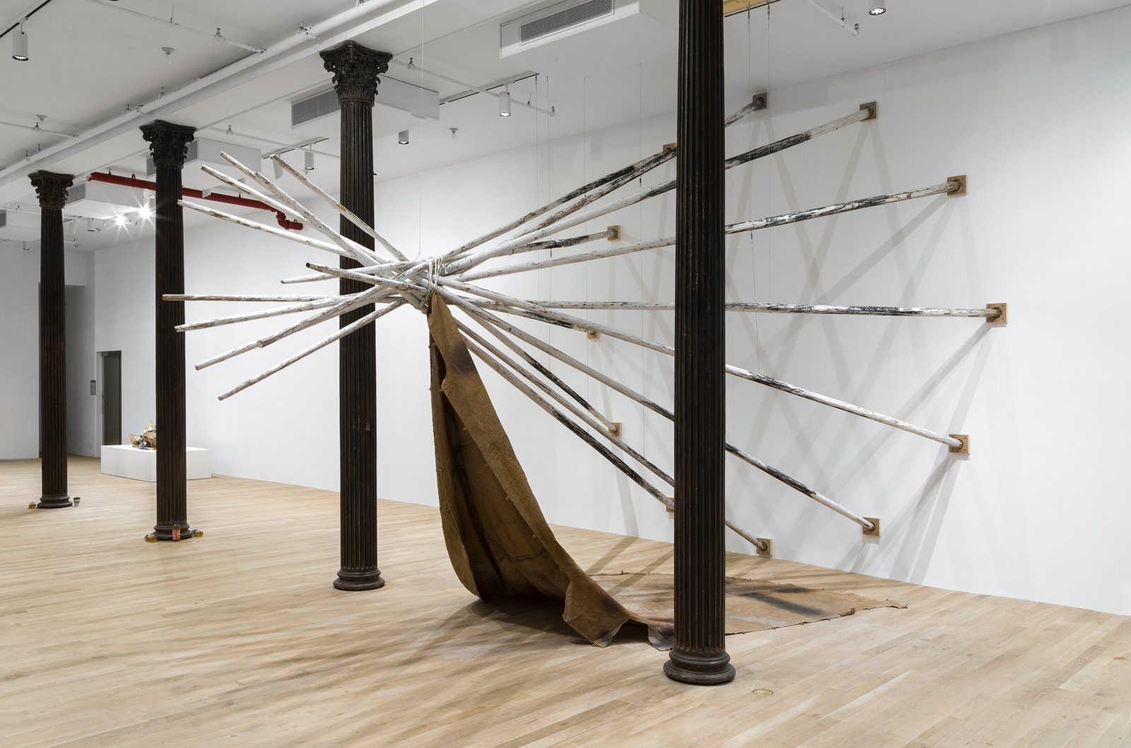 Duane Linklater, dislodgevanishskinground, 2019, 12 tipi poles, steel cable, white paint, charcoal, rope, digital print on linen, black tea, blueberry extract, sumac, charcoal, 220 x 174 x 174 in. (559 x 442 x 442 cm). Installation view, Artists Space, New York, USA, 2019