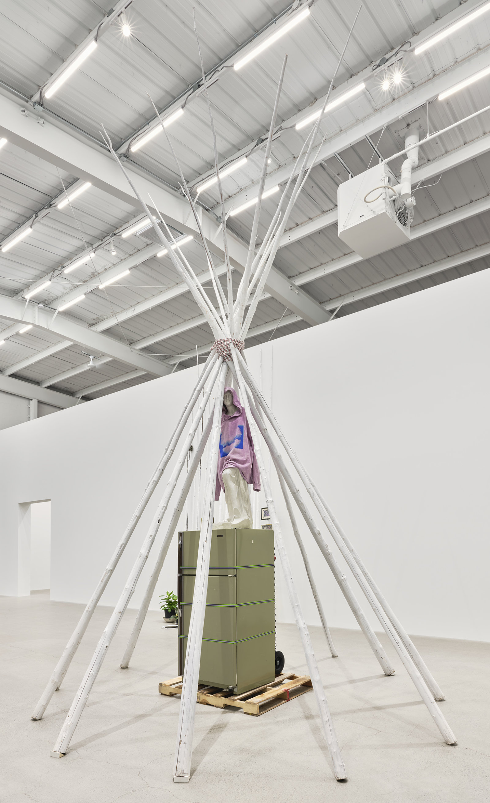 Duane Linklater, what grief conjures, 2020, tipi poles, paint, nylon rope, wooden pallet, refrigerator, tie-down straps, hand truck, plastic statue, handmade hoodie, cochineal dye, silkscreen, 249 x 160 x 160 in. (632 x 406 x 406 cm)