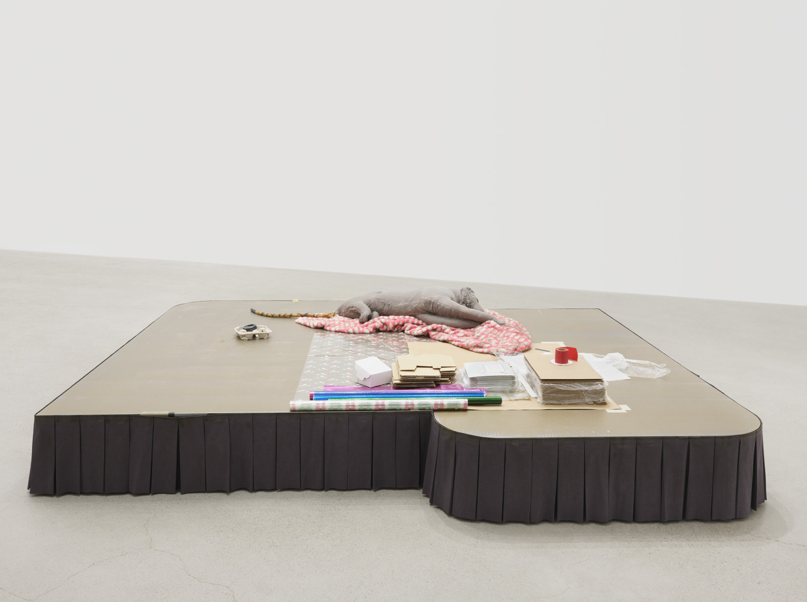 Liz Magor, Shaved, 2020, painted plywood, fabric skirting, silicone rubber, faux fur, toy tail, packaging materials, 23 x 120 x 109 in. (58 x 305 x 277 cm)