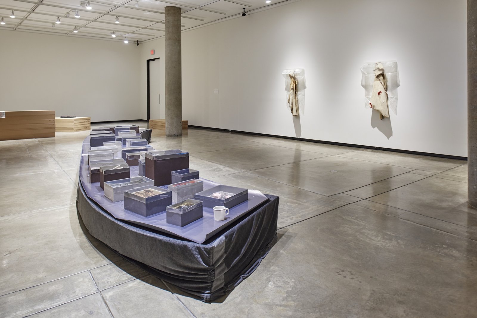 Liz Magor, Shoe World, 2018, 33 pairs of secondhand shoes, mat-board shoeboxes of variable dimensions with polyester film lids, porcelain mug, coffee, and plywood platform with fabric cover, 12 x 288 x 40 in. (31 x 732 x 102 cm). Installation view, BLOWOUT, Carpenter Center for Visual Arts, Cambridge, USA