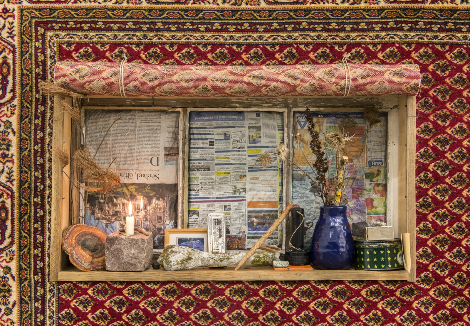 Ashes Withyman, Pensione from a place, near the buried canal (detail), 2011–2012, carpet, cow bone, candle, stone, fungus, harmonica, pine branch, string, clothes peg, flashlight, tin, matches, paper, window, newspaper, 80 x 106 x 10 in. (203 x 269 x 25 cm)