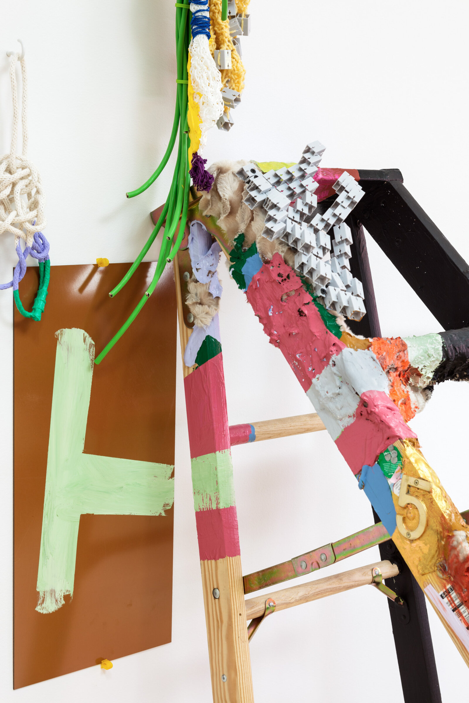 Jessica Stockholder, A - H (detail), 2013, ladder, brass, plastic toy modules, yarn, string, extension cord, plexiglas, rope, acrylic paint, fake fur, cardboard, zip ties, TV mount, white hook, hardware, 85 x 27 x 49 in. (215 x 69 x 125 cm)