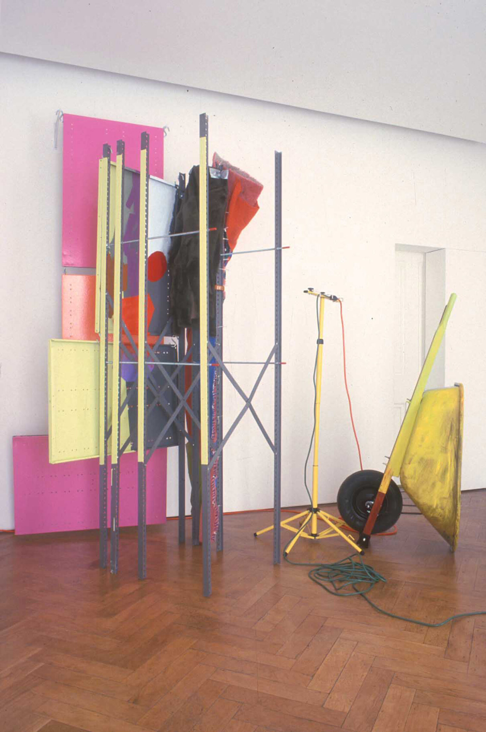 Jessica Stockholder, Coupling, 1998, metal shelving elements, threaded rod, carpet, fur, blankets, clothing, oil-based enamel paint, oil paint, acrylic paint, wheel barrow, light stand, extension cords, rope, hardware, brass and wooden threshold plates, space heater with fan, 166 x 149 x 111 in. (422 x 378 x 281 cm)